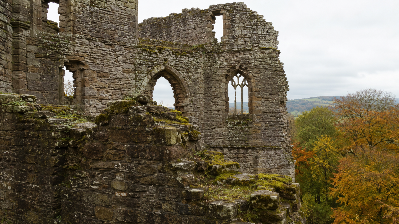 Moss-covered ruined castle walls with empty window arches surrounded by autumn trees