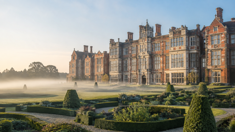 A grand Tudor-style English castle palace with tall mullioned windows and ornate chimneys overlooking manicured gardens